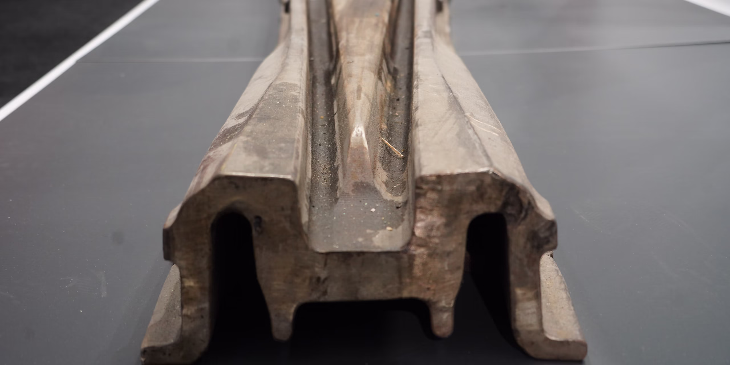 Why exhibit Close-up front view of a cut cross-section of a rail profile with central groove, lying on a table.